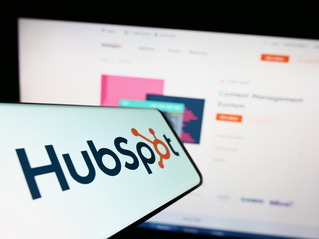 Telefono con logo de HubSpot sobrepuesto en pantalla de computadora